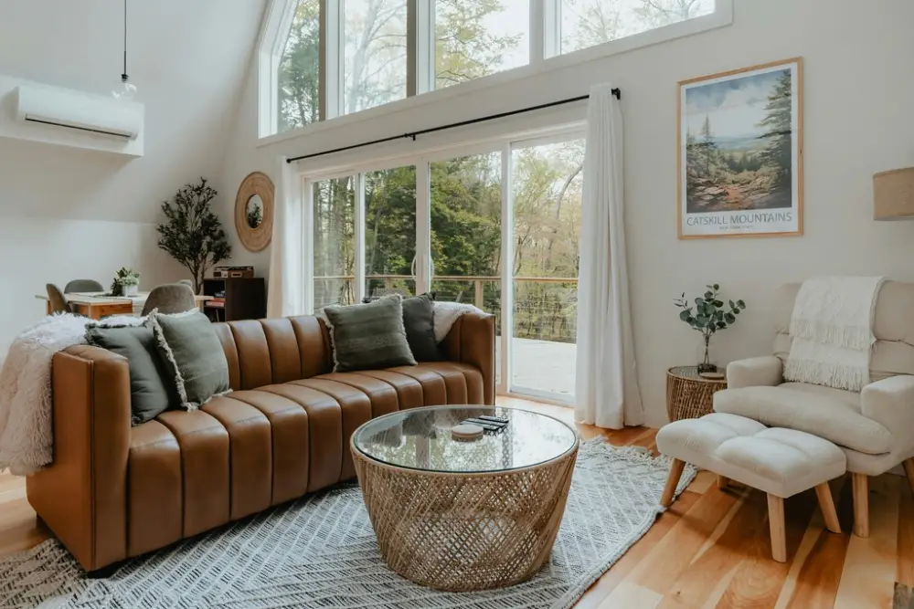 A bright, airy living room with large windows that let in natural light. The walls are painted a soothing shade of white, and the floors are a warm hardwood.